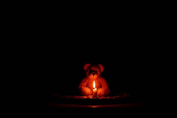 istock Brown little teddy bear sitting on table by candle flame 2170242101