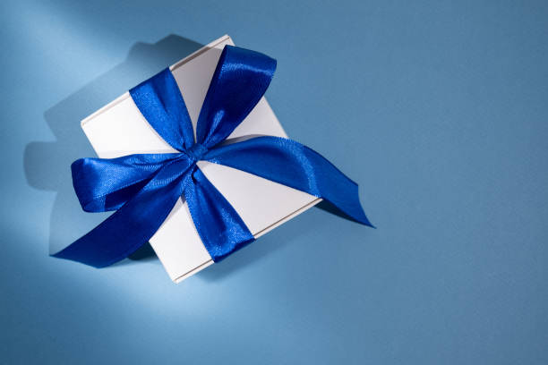 istock White box with blue bow and ribbons on a colored background. Gift box 2170244552