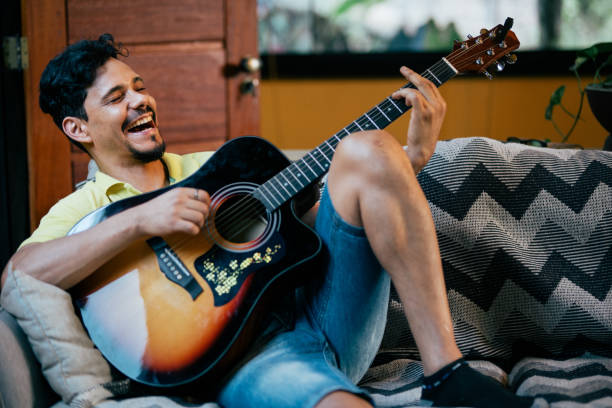 istock Young man playing guitar sitting on the couch 2170245408