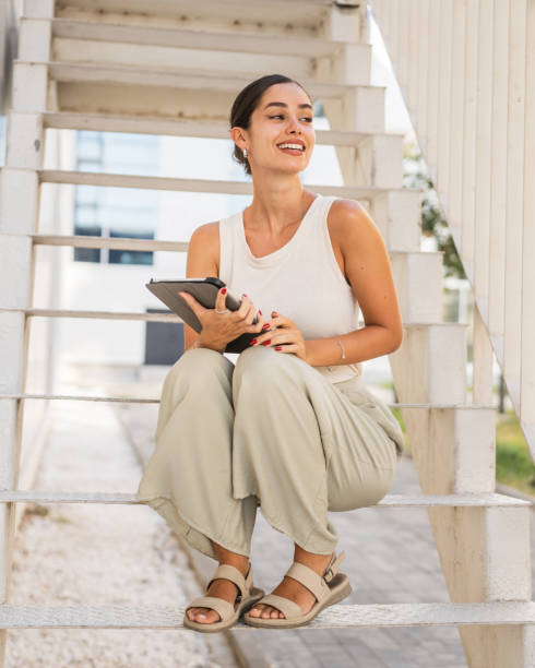 istock Young happy woman sit on stairs and use digital tablet 2170246255