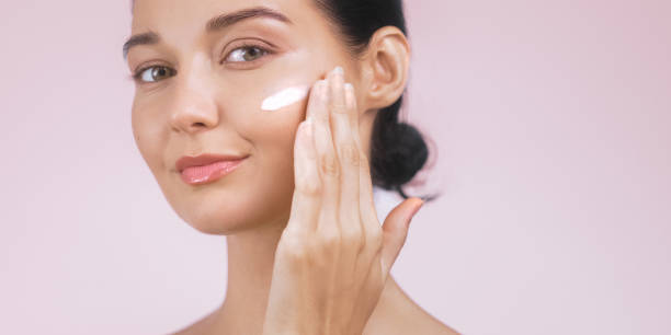 istock Young Woman Applying Face Cream on Soft Pink Background with Copy Space 2170253851