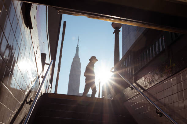 A man in a fedora walks by the 34th street subway station near the Empire State Building, silhouetted by the morning sun