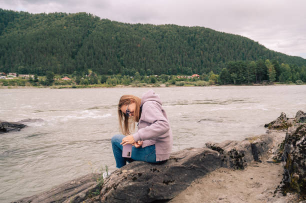 Woman at the river Katun at summer day. Taking photo on her smartphone