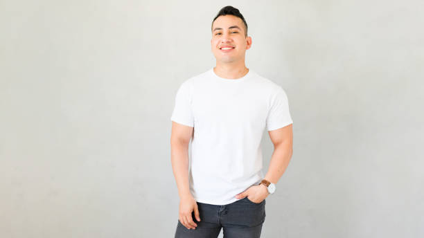 istock Smiling young man in blank white t-shirt with hand in pocket standing against plain grey background 2170270399