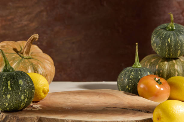 Autumn comfort visualized. Green and red pumpkins, lemons and tomatoes decorate around a wooden panel on a brown vintage background. Empty space for display product