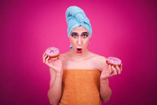 istock A funny guy dressed as a drag queen and eating pink donuts. Pink background. 2170281712