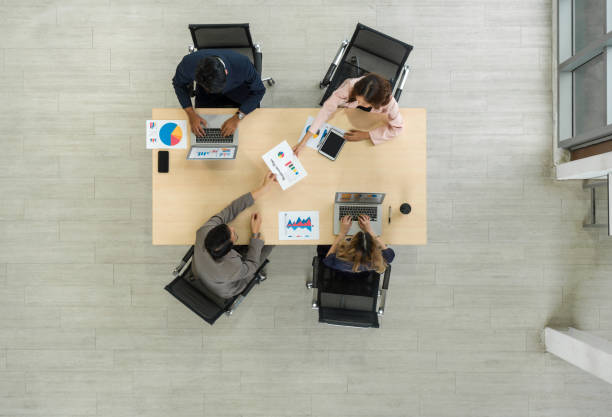 istock A team of workers is seated together at a big table in an office, sharing thoughts and talking. Top view 2170282757