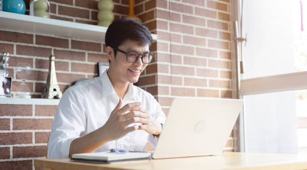 istock close up new graduated asian man talking or answer question by video conference call with reviewer (HR) for introduce and do job interview online in living room at house for we're hiring concept 2170283208