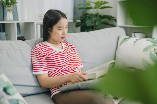 istock A relaxed young woman enjoy reading a book on a sofa at home. 2170287328