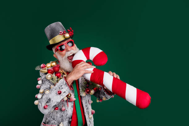 istock Portrait of eccentric man bite large candy cane pillow blazer decorated xmas tree toys isolated on dark green color background 2170292011