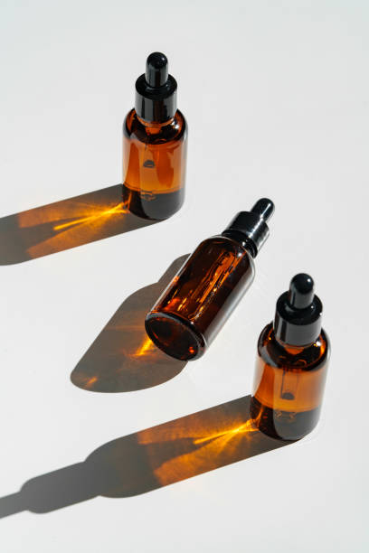 istock Arranged Amber Glass Bottles With Droppers on White Surface Accentuated by Shadows in Bright Light 2170292125