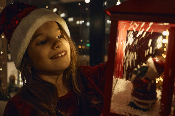 Beautiful girl on a New Year’s Eve looking at lantern with fake snow, dreaming about future.