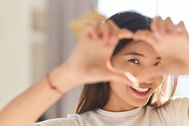 istock Smiling Woman Framing Heart Shape With Hands In Bright Natural Light 2170297668