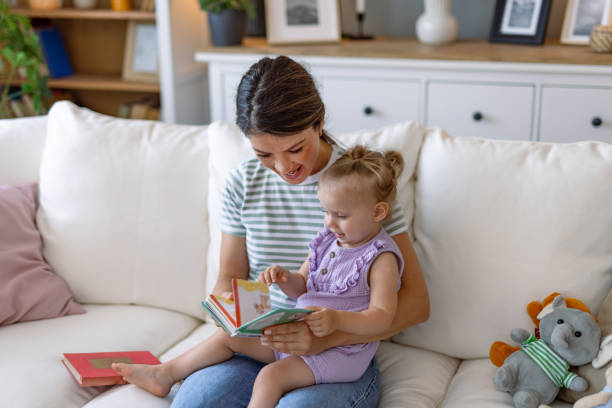istock Mother reading a book to her daughter on the couch. 2170299817