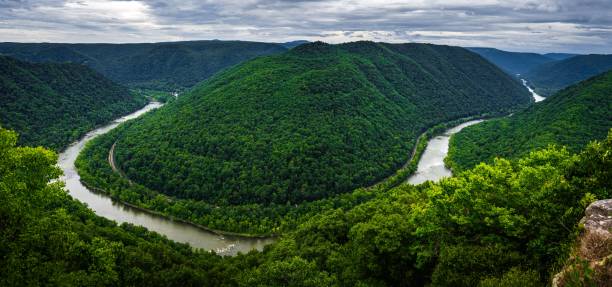 Panoramic view of the New River Gorge in West Virginia with lush green mountains and a winding river under a cloudy sky.