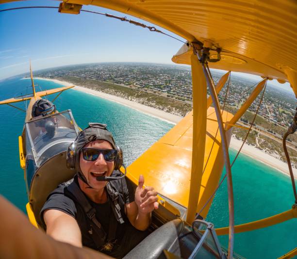 A man takes a selfie from aboard a yellow biplane.