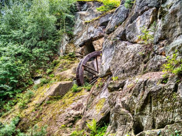 An old water wheel embedded in a rocky cliff surrounded by lush green forest.