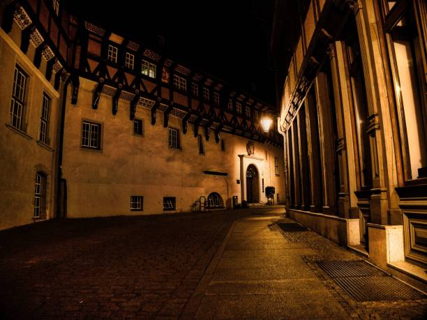 Nighttime view of a historic building with a lit street lamp casting warm light on the cobblestone street.