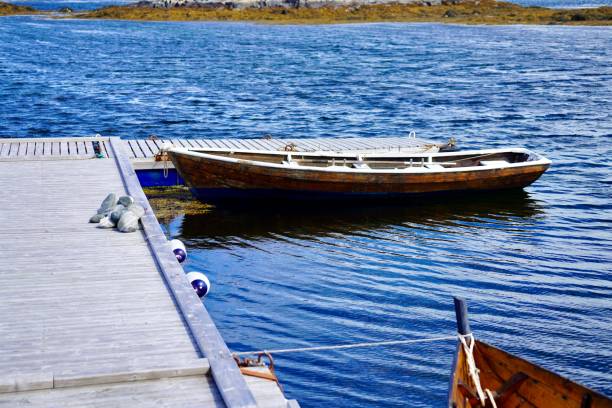 A wooden boat docked at a pier on a clear day with calm blue waters and a rocky shoreline in the background.
