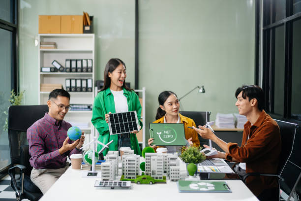 istock Asian professionals collaborate on sustainable energy solutions with wind turbines, solar panels, and eco friendly models 2170306056