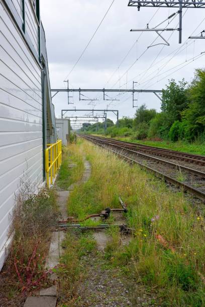 istock Overgrown railway trackside next to a white building and overcast sky. 2170308047