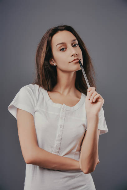istock Young woman holding pen and thinking on grey background 2170310433