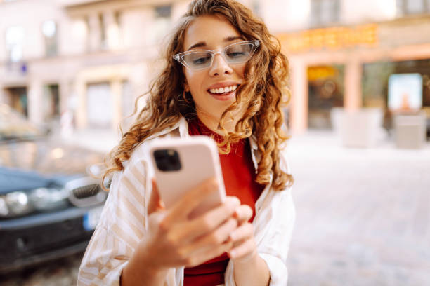 istock Young woman enjoying a sunny day while using her phone in a vibrant urban setting with stylish sunglasses and a cheerful expression. 2170310768