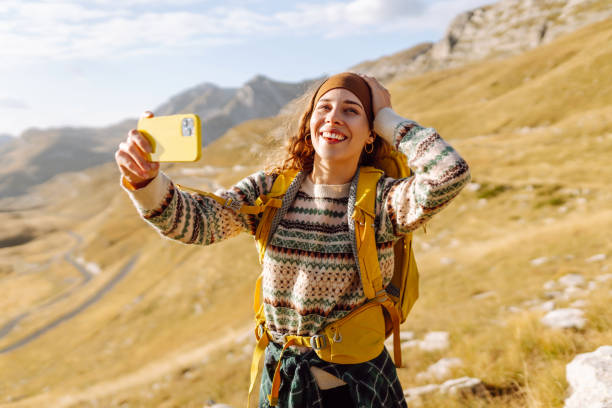 istock A young woman with a backpack is happily taking a selfie in the mountains. 2170313838