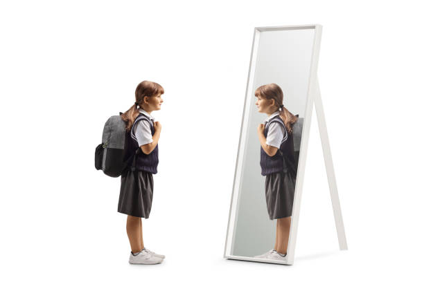 istock Girl in a school uniform standing with a backpack on shoulders and looking at a mirror 2170316032