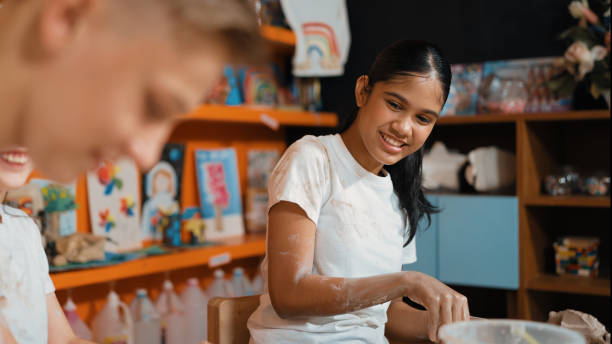 istock Girl modeling cup of clay while children laughing at art class. Edification. 2170334838