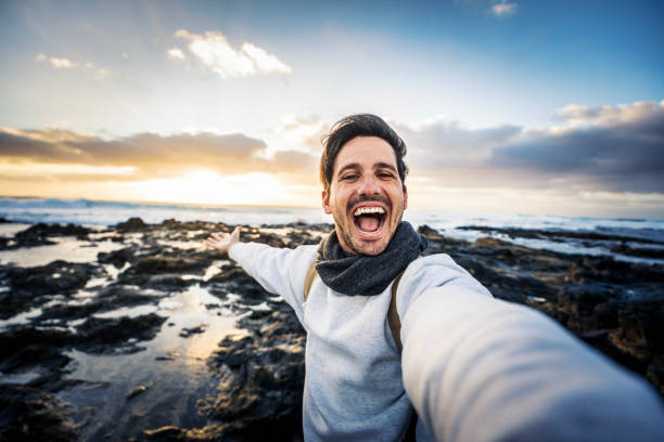 istock Handsome young man taking selfie pic with smart mobile phone outdoors - Traveler guy smiling at camera with sunset on background - Traveling life style and technology concept 2170336657