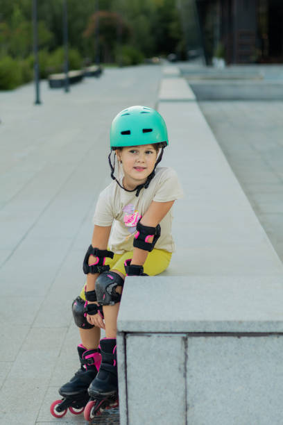 istock Beautiful playful school girl with protective equipment and helmet on inline rollerblade skates in public park near the corporate building. 2170341338