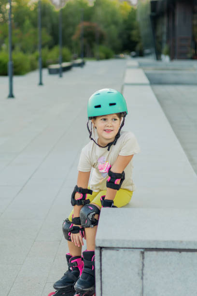 istock Beautiful playful school girl with protective equipment and helmet on inline rollerblade skates in public park near the corporate building. 2170342588