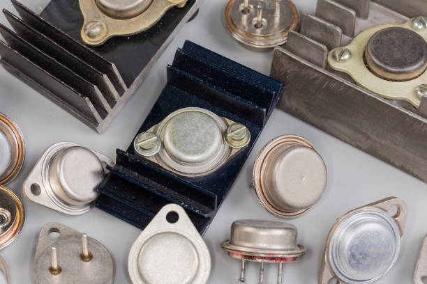 Old bipolar power transistors various purpose in metal packages, some of them installed on finned passive heatsinks on a gray surface, fragment close-up