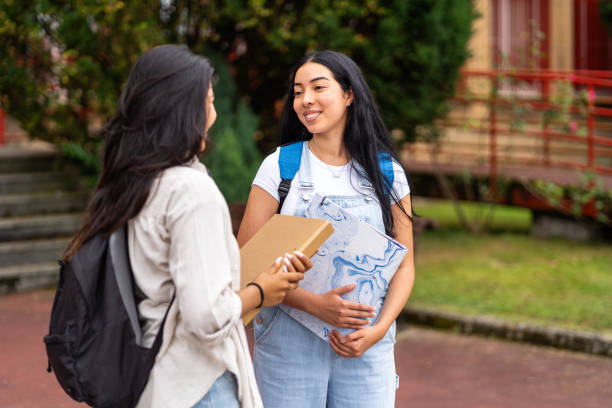 istock Two hispanic students chat on a college campus, carrying books and sporting backpacks 2170345316