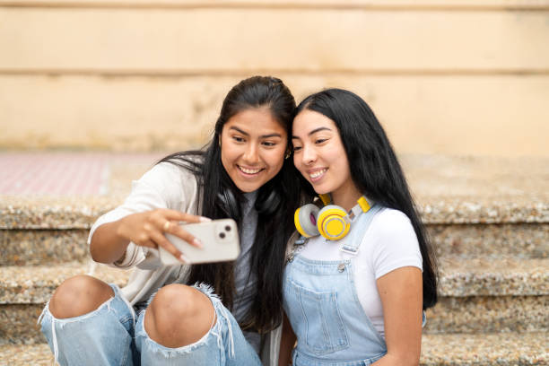 istock Two happy hispanic students are taking a selfie with a phone while sitting on campus stairs 2170345323