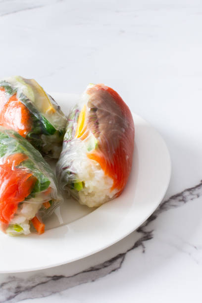 These traditional Vietnamese spring rolls feature rice paper filled with lettuce, salmon, carrots, and cucumber, served with fish sauce, offering a light and flavorful appetizer These traditional Vietnamese spring rolls feature rice paper filled with lettuce, salmon, carrots, and cucumber, served with fish sauce, offering a light and flavorful appetizer