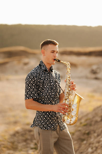 istock A young man joyfully plays the saxophone outdoors in a picturesque setting, surrounded by nature at sunset 2170351293
