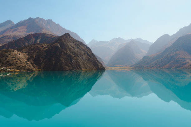 A tranquil turquoise lake mirrors the towering mountains around it, creating a stunning landscape. The calm water and clear skies invite relaxation and contemplation in nature's embrace.