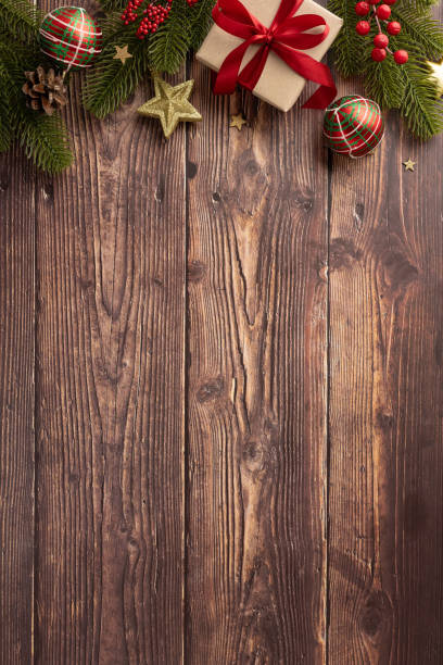 istock Festive vertical Christmas scene featuring a beautifully wrapped gift with red ribbon surrounded by pine branches and ornaments on a rustic wooden background 2170375006