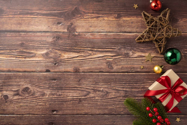 istock Festive Christmas decorations on rustic wooden background. Includes a gift box with a red ribbon, star ornament, and festive baubles 2170375020