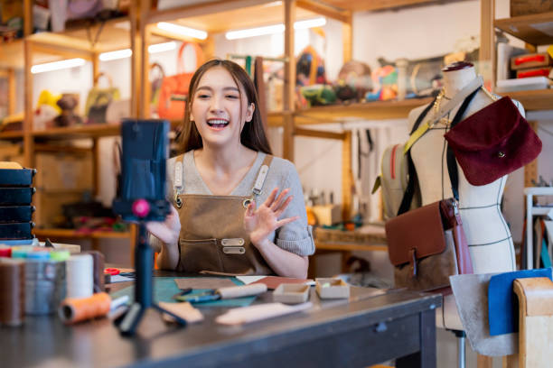 istock Leather bag making online course, asian female craft person influencer teaching how to make leather work bag online ,she is talking to student on smartphone lives online course 2170379720