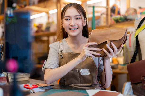 istock Leather bag making online course, asian female craft person influencer teaching how to make leather work bag online ,she is talking to student on smartphone lives online course 2170379736