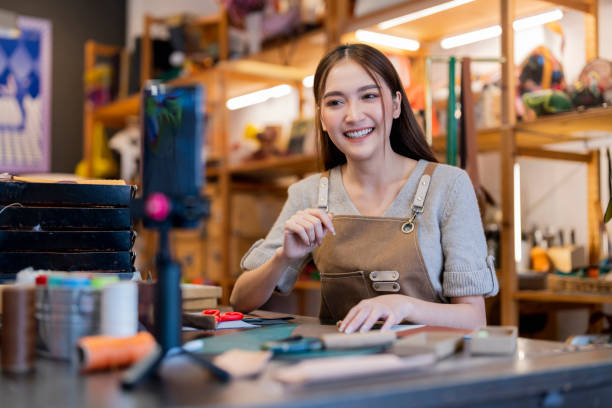 istock Leather bag making online course, asian female craft person influencer teaching how to make leather work bag online ,she is talking to student on smartphone lives online course 2170379740