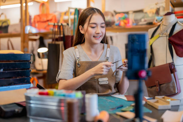 istock Leather bag making online course, asian female craft person influencer teaching how to make leather work bag online ,she is talking to student on smartphone lives online course 2170379747