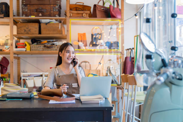 istock leather shop leather bag designer talking to customer smartphone checking order with laptop business female owner working in home studio handcraft product 2170380090