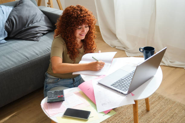 istock Smiling young woman taking notes while studying online at home 2170383877