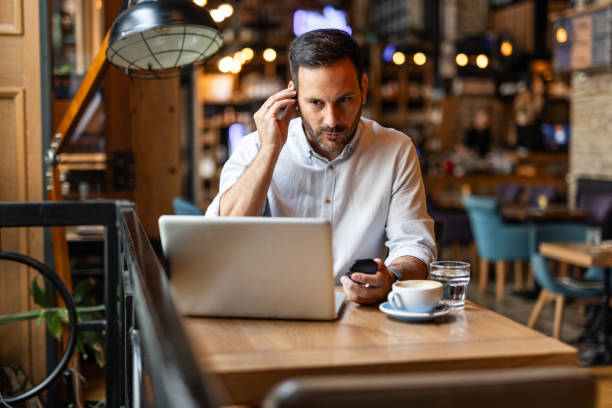 istock Satisfied modern business man in stylish clothes sitting in cafe using smartphone and headphones 2170385408