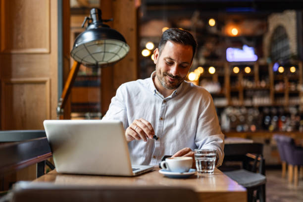 istock Satisfied modern business man in stylish clothes sitting in cafe using smartphone and headphones 2170385465
