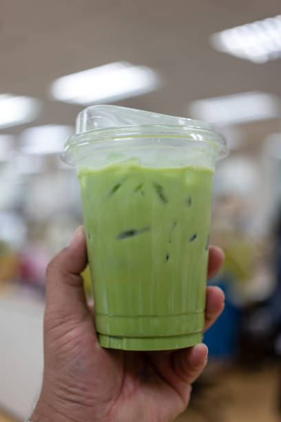 Hand holding the glass iced matcha latte green tea. Drinking menu.